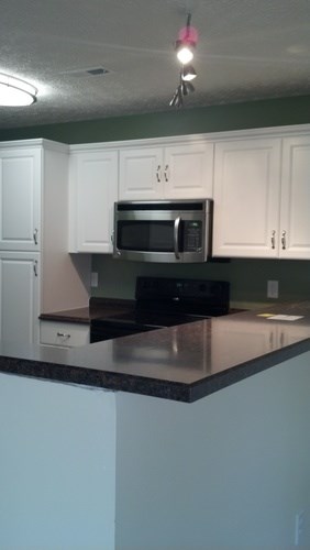 A kitchen with white cabinets and a black microwave.