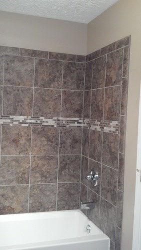 A white bathtub sits under a tile wall.