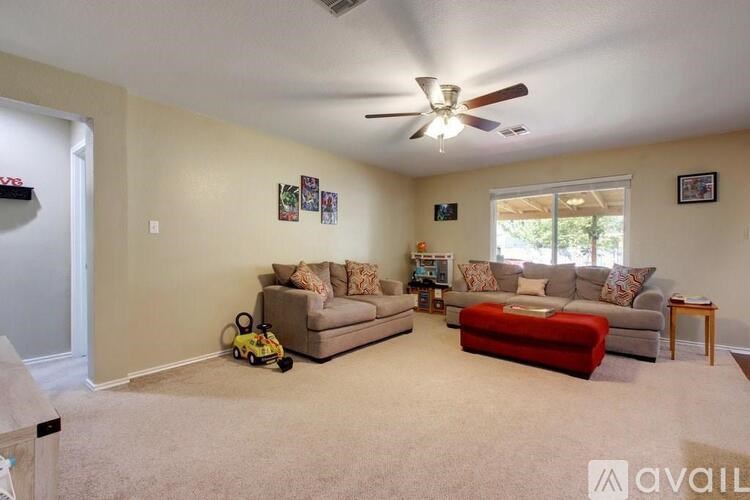 A living room with a ceiling fan and a red ottoman.