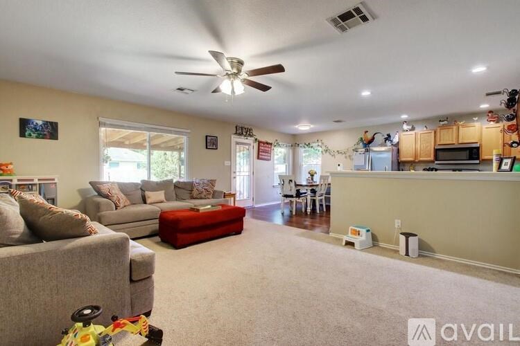 A living room with a grey couch, a red ottoman, and a ceiling fan.
