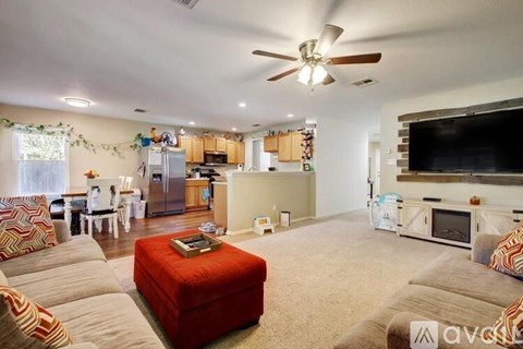 A living room with a red ottoman and a television on the wall.