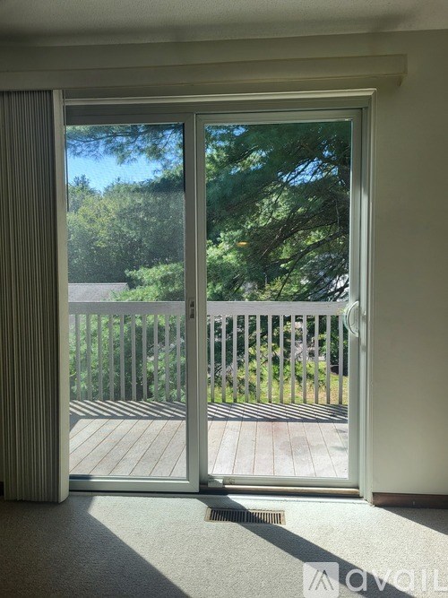 A sliding glass door with a view of a deck and trees outside.