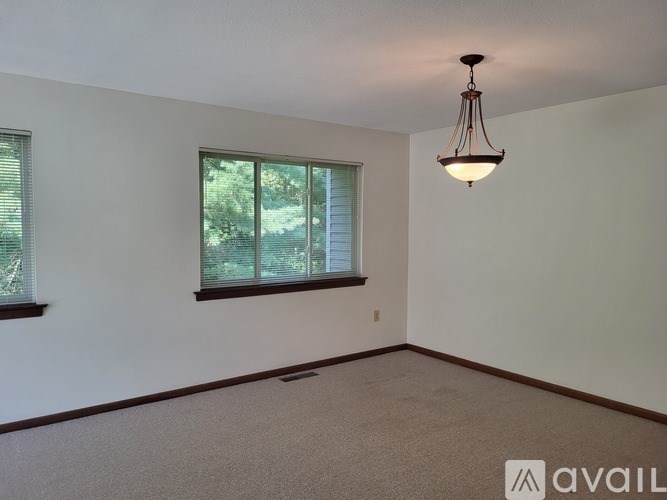 A room with a carpeted floor, a window with blinds, and a hanging light fixture.