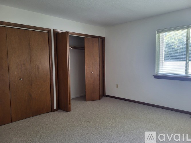 A room with a carpeted floor, two wooden doors, and a window with blinds.