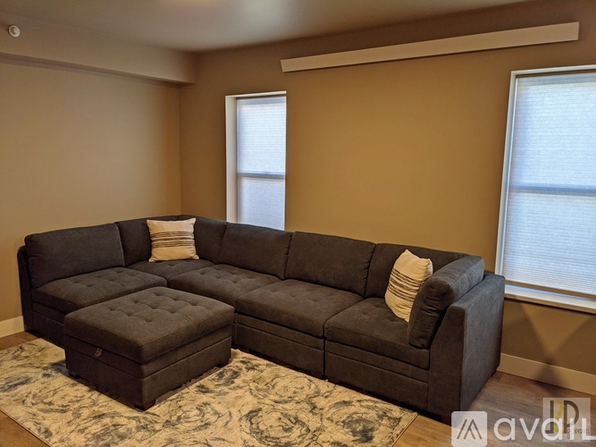 A grey sectional sofa with a chaise lounge and ottoman in a room with a rug and two windows.