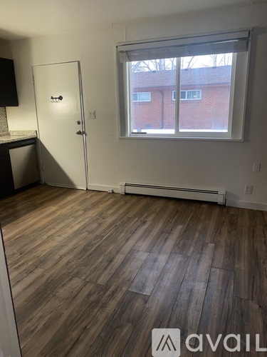 A room with wooden flooring and a window overlooking a red brick building.