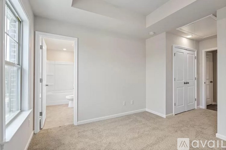 A white bedroom with a carpeted floor and a window on the left.