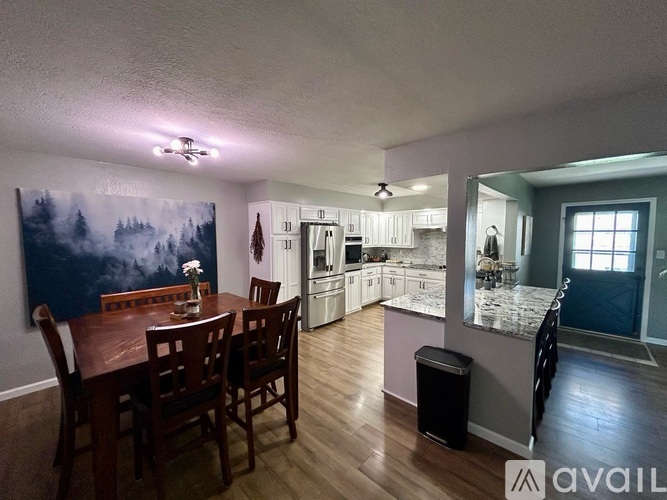 A kitchen with a dining table and chairs in the foreground and a painting on the wall.