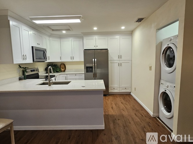 A modern kitchen with white cabinets and a wooden floor.
