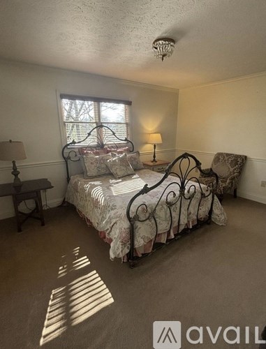 A bedroom with a bed, chair, and window.