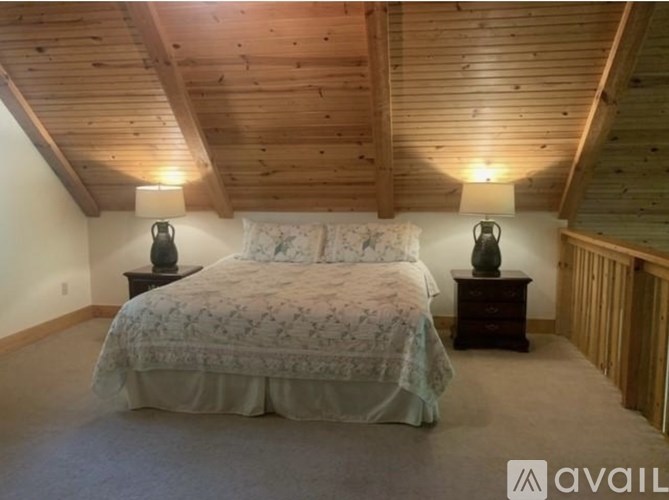 A bedroom with a bed, two lamps, and a wooden ceiling.