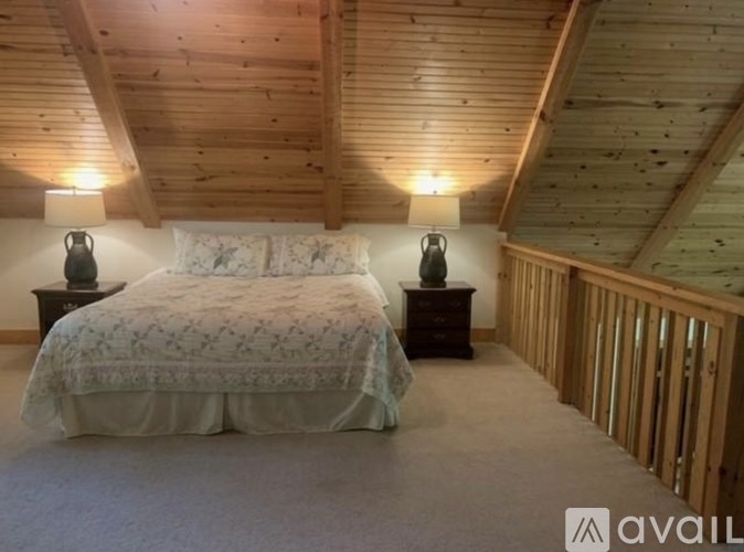 A bedroom with a bed, two lamps, and a wooden ceiling.