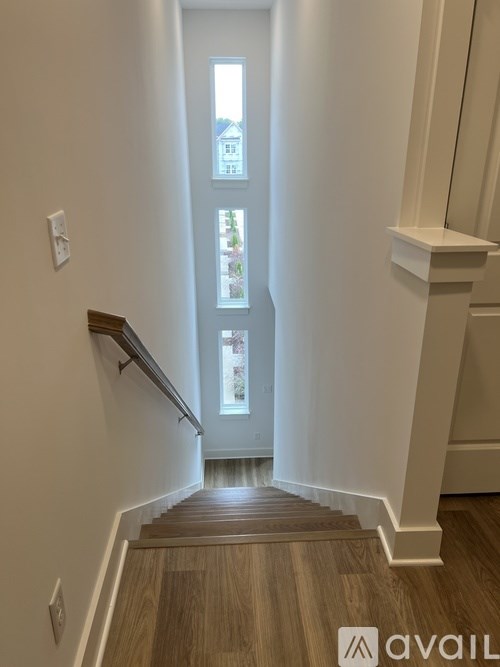 A staircase with wooden steps and a white railing leads to a bright room with a window.
