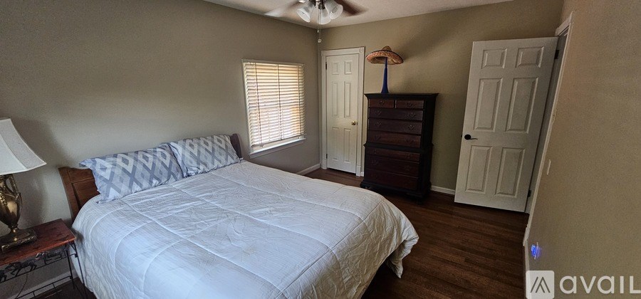 A bedroom with a large bed and a dresser with a lamp on it.