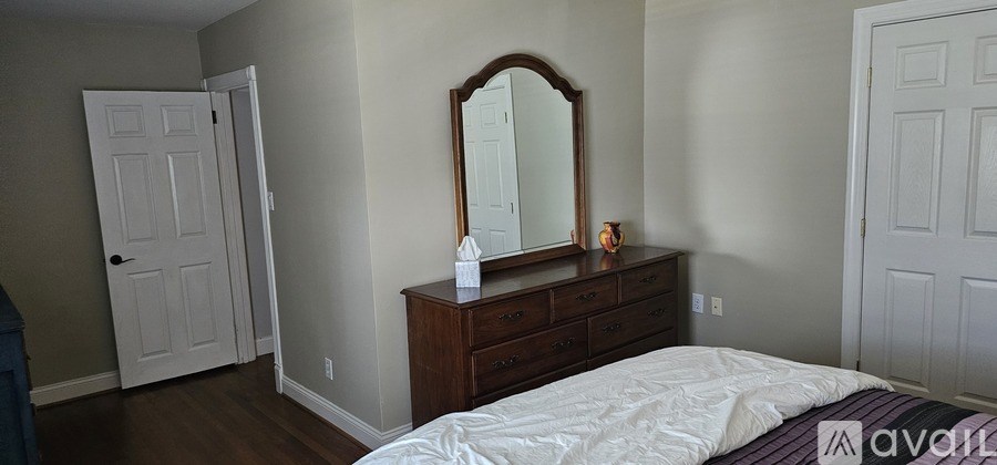 A bedroom with a bed, dresser, mirror and two doors.