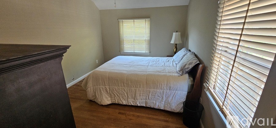 A bedroom with a bed, nightstand, and window with blinds.