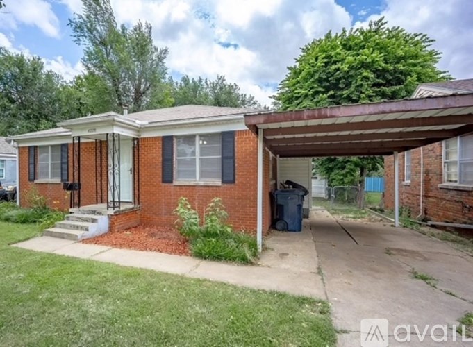 A small red brick house with a porch and a covered driveway.
