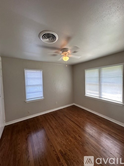 A room with a ceiling fan and two windows.