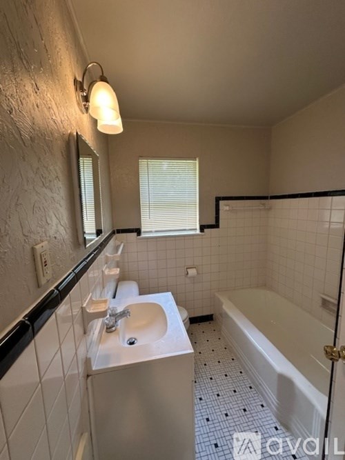 A white sink with a black counter top and a white bathtub with black and white tiles.