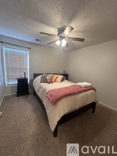 A bedroom with a bed, ceiling fan, and window with blinds.