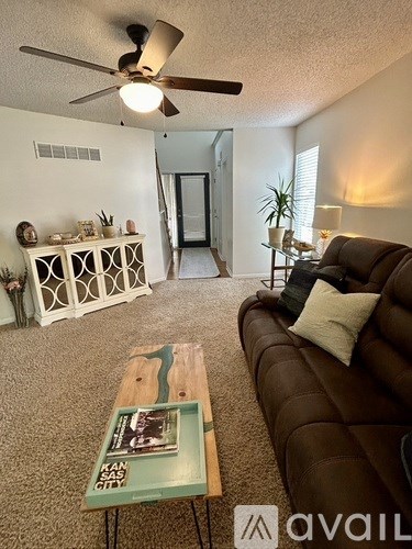 A living room with a brown couch, a green coffee table, and a ceiling fan.