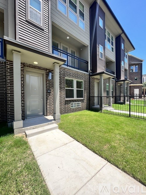 A modern two-story apartment building with a balcony and a small front yard.