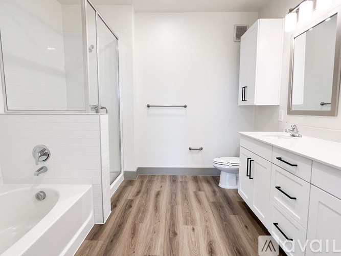 A white bathroom with wood flooring and a glass shower door.