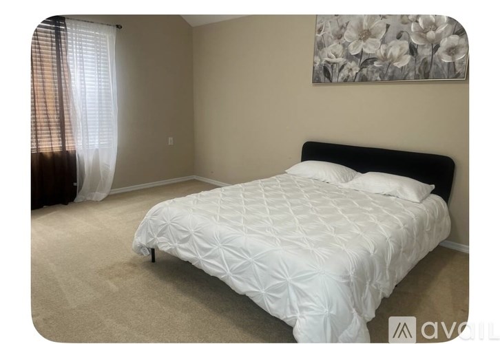 A bedroom with a white bedspread and a floral picture on the wall.