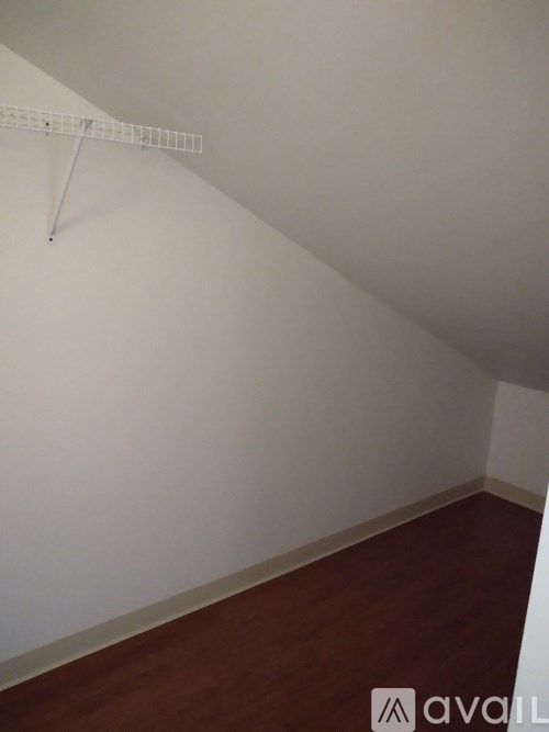 A white wall with a wooden floor and a white shelf on the wall.