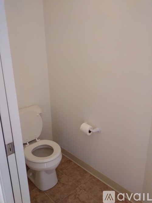 A white toilet with a roll of toilet paper on the wall.