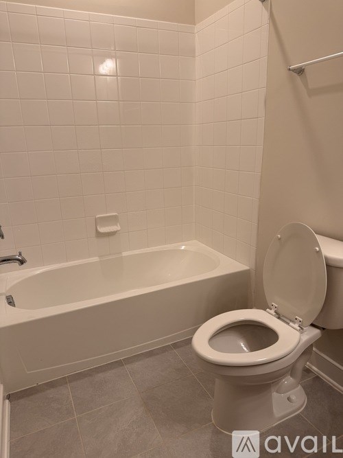 A white toilet in a bathroom with a white bathtub and white tiles.
