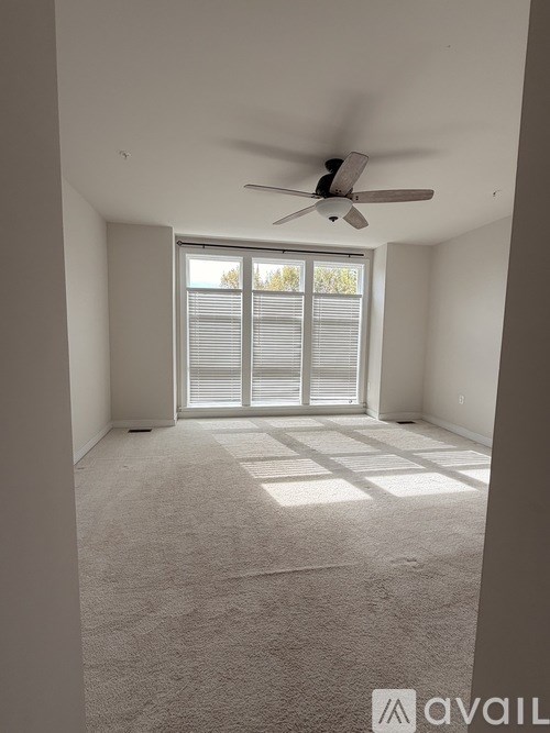 A room with a ceiling fan and a large window with blinds.