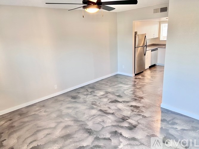 A room with a ceiling fan and a kitchen in the background.