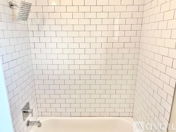 A white tiled bathroom with a white tub and shower head.