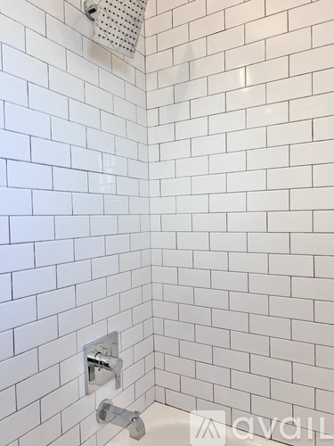 A white tiled shower with a silver faucet.
