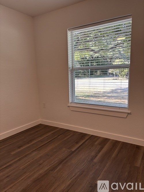 A room with wooden flooring and a window showing a view of a street.