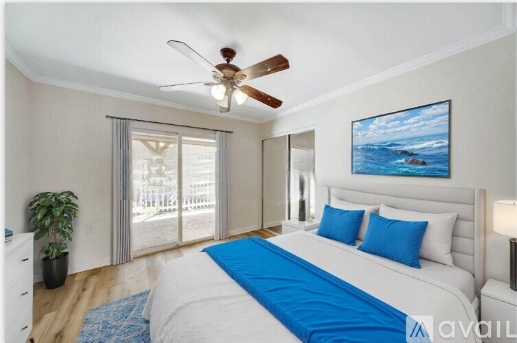 A bedroom with a bed, a ceiling fan, and a painting of a beach scene on the wall.