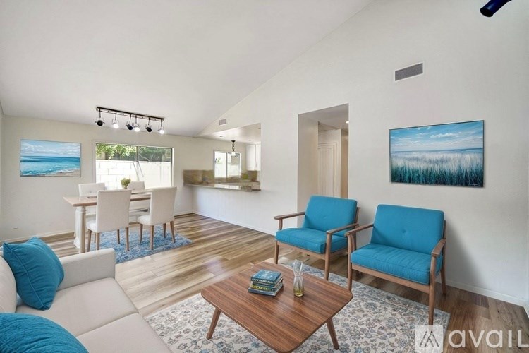 A living room with a blue chair and a painting of a beach scene on the wall.