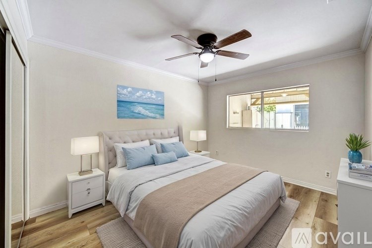 A bedroom with a bed, a ceiling fan, and a painting on the wall.