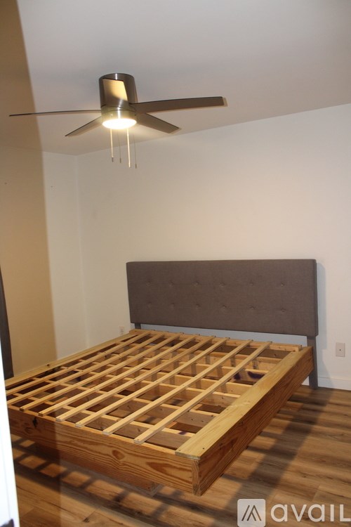 A bed with wooden slats and a grey headboard is in a room with a ceiling fan.
