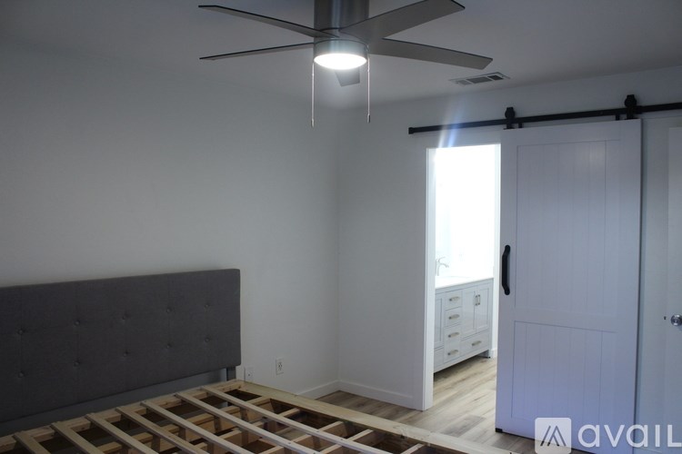 A room with a ceiling fan and a bed with wooden slats on the floor.