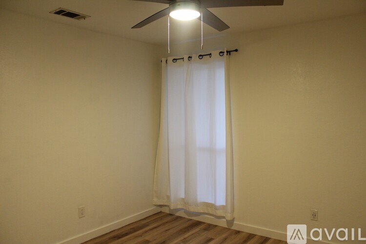 A room with a ceiling fan and a window with curtains.