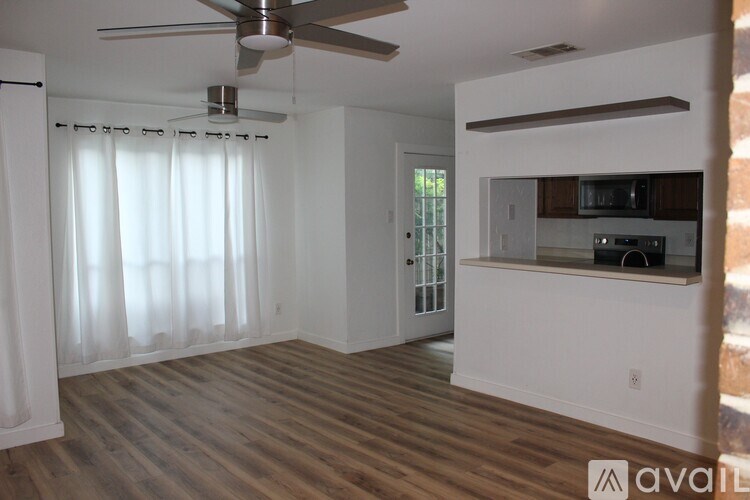 A spacious living room with a ceiling fan and a kitchenette in the background.