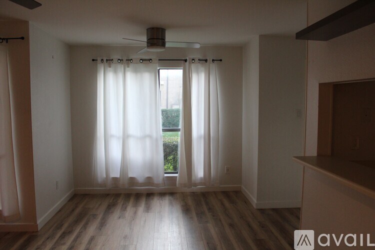 A room with a fan, curtains, and wooden floors.