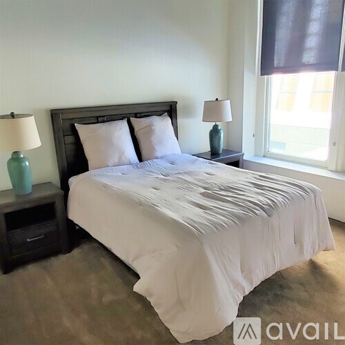A bed with white bedding and a dark headboard is in a room with a window.