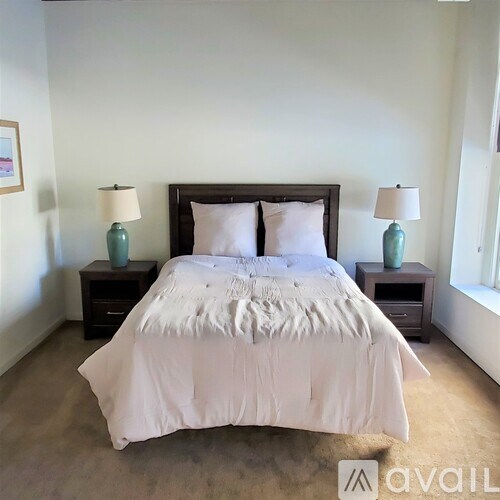 A bed with white bedding sits in a room with two lamps on either side.