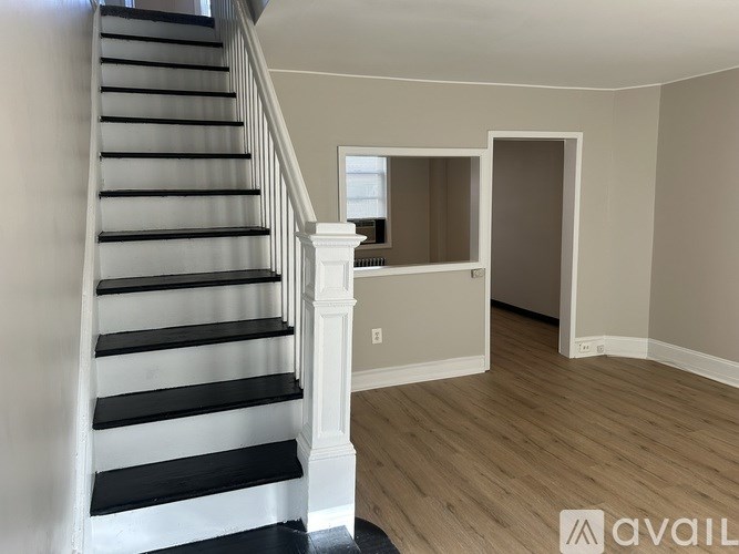 A staircase with black steps and white railings leads to an empty room with a window.