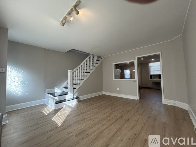 A spacious room with wooden flooring and a staircase leading to another room.