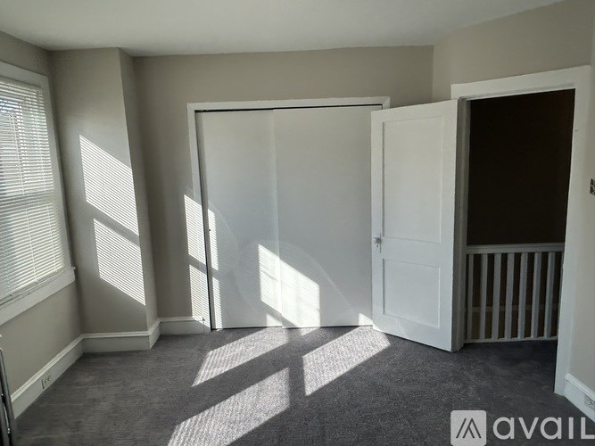 A room with a carpeted floor, a white door, and a window with blinds.