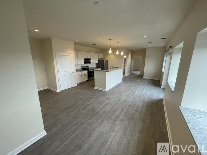 A spacious, empty room with wooden flooring and a kitchen area in the background.